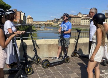 A group gathers on a bridge in Florence, Italy along with their e-scooters