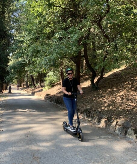 a man rides an e-scooter through a tree-lined area in Florence, Italy