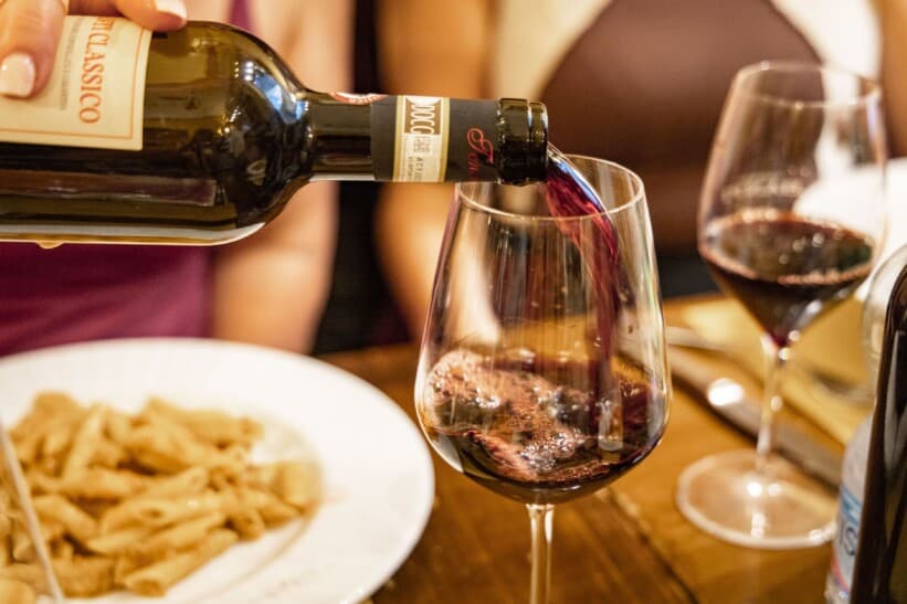 A glass of red wine is poured alongside a plate of pasta
