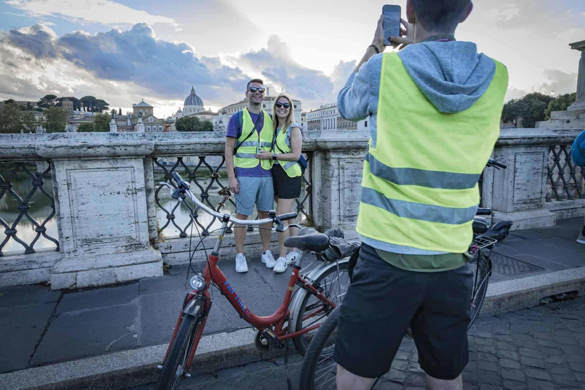 A couple poses for a photo on a bridge in Rome with St. Peter's Basilica in the background