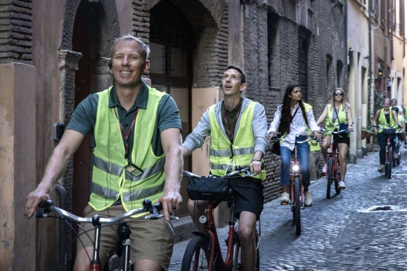 A group of cyclists rides through a cobblestone street in Rome, Italy