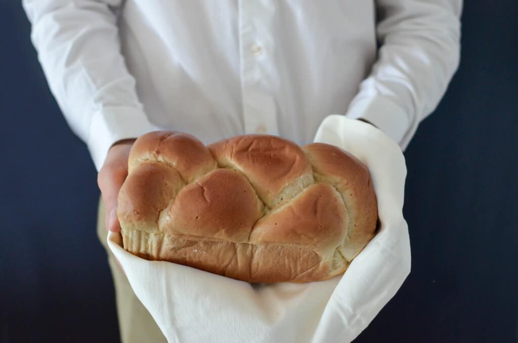 Braided bread held in person's hands and they are wearing a white shirt
