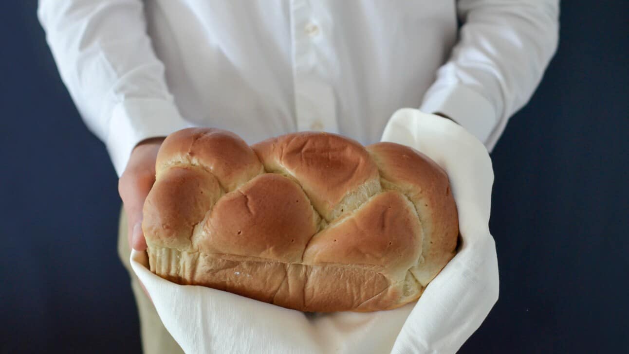 Braided bread held in person's hands and they are wearing a white shirt