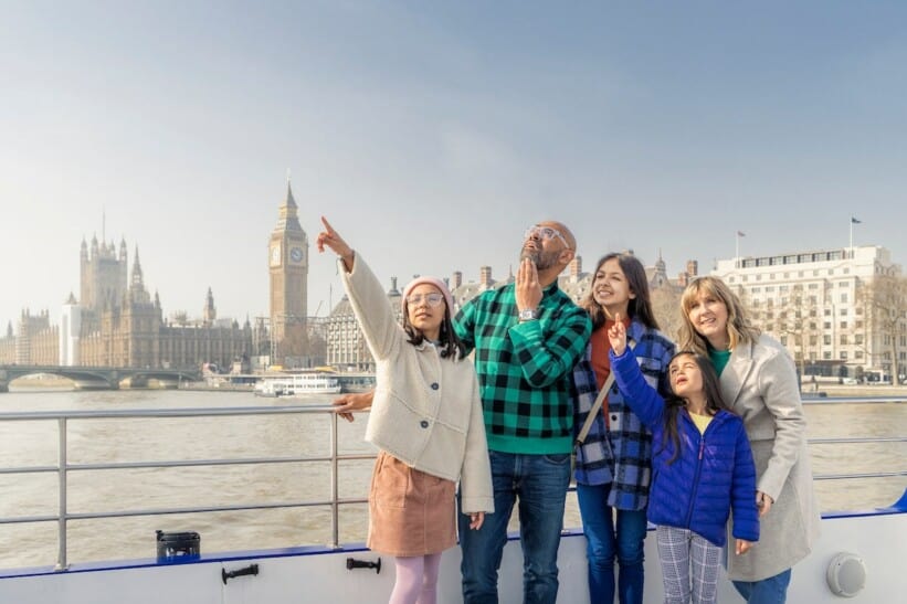 A family points to London landmarks from a river cruise along the Thames with Big Ben and Parliament in the background