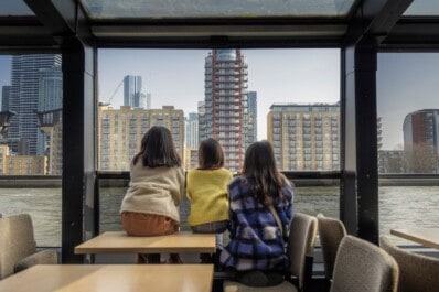 Three girls admire the London cityscape from a boat on the Thames