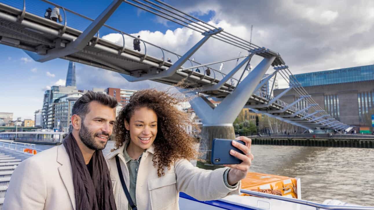 A couple takes a selfie in front the Millennium Bridge in London while on a River Thames cruise