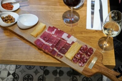 A planche of charcuterie and cheese with olives, tapenade, and wine
