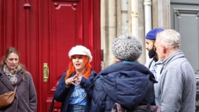 A tour guide explains the surroundings to the group as she stands in front of a red door