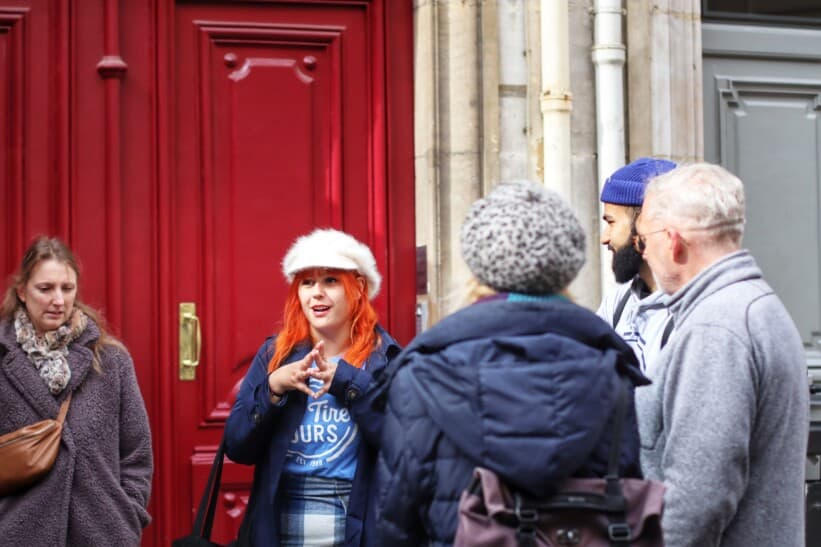 A tour guide explains the surroundings to the group as she stands in front of a red door