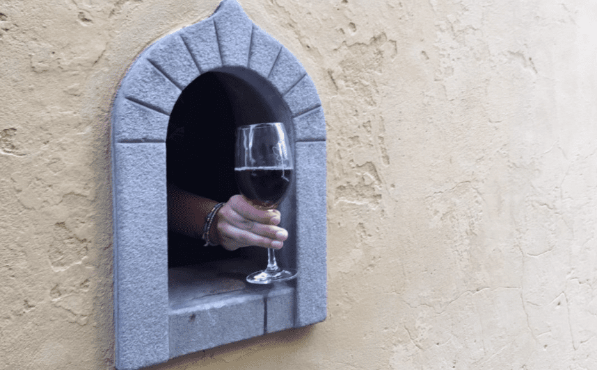 A hand coming out of a Florence wine hole with a glass of red wine.