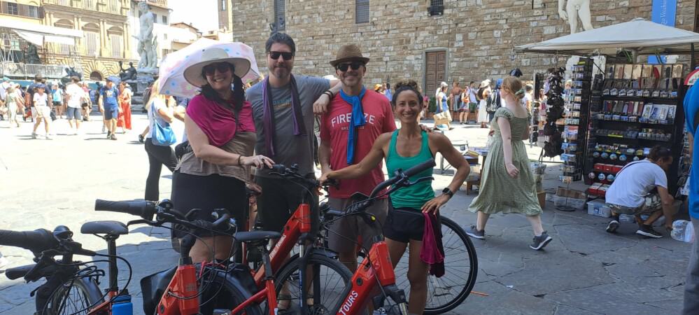A group of four poses for a photo with red e-bikes in Florence