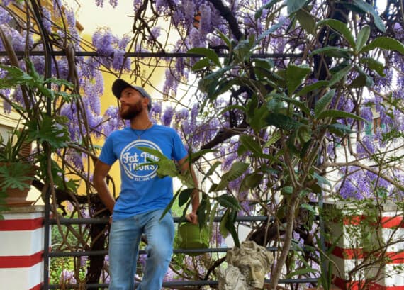 A male in a blue t-shirt sitting among purple bushes.