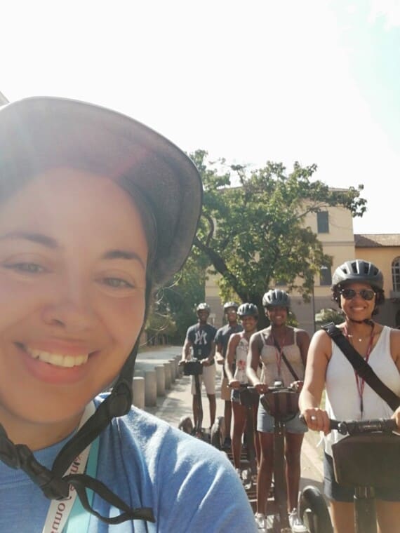 A female tour guide takes a selfie with her group on Segways in the background.