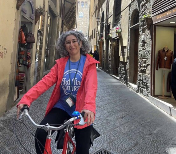 A woman on a bicycle on a small street in Florence.