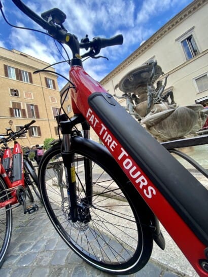 A red Fat Tire Tours e-bike parked next to a fountain