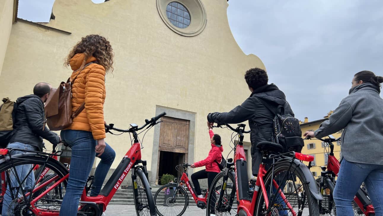 A group of cyclists on e-bikes learn about the Santo Spirito church in Florence, Italy