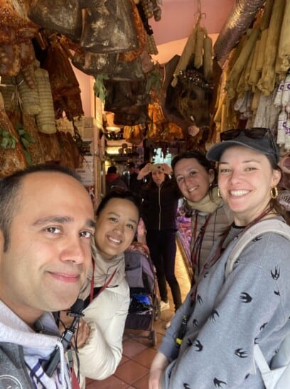 A group of friends in a butcher's shop standing among dried sausages