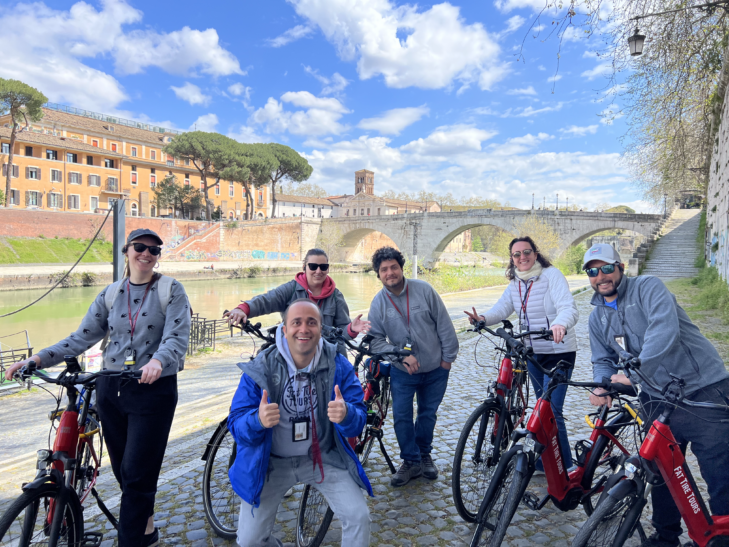 A group of cyclists pose for a photo alongside the river in Rome, Italy