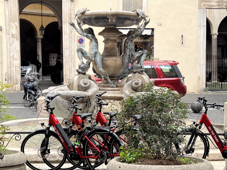 Red e-bikes parked beside a fountain in Rome, Italy