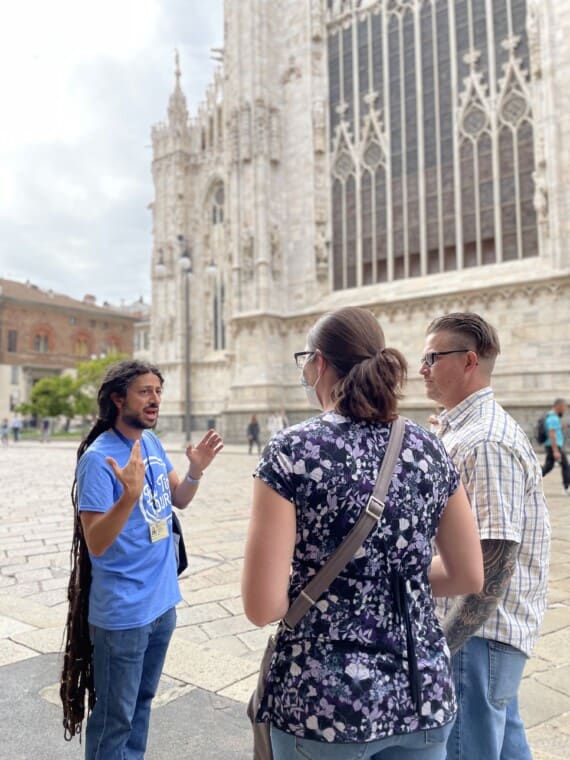 A tour guide addresses two guests in front of the Milan Cathedral