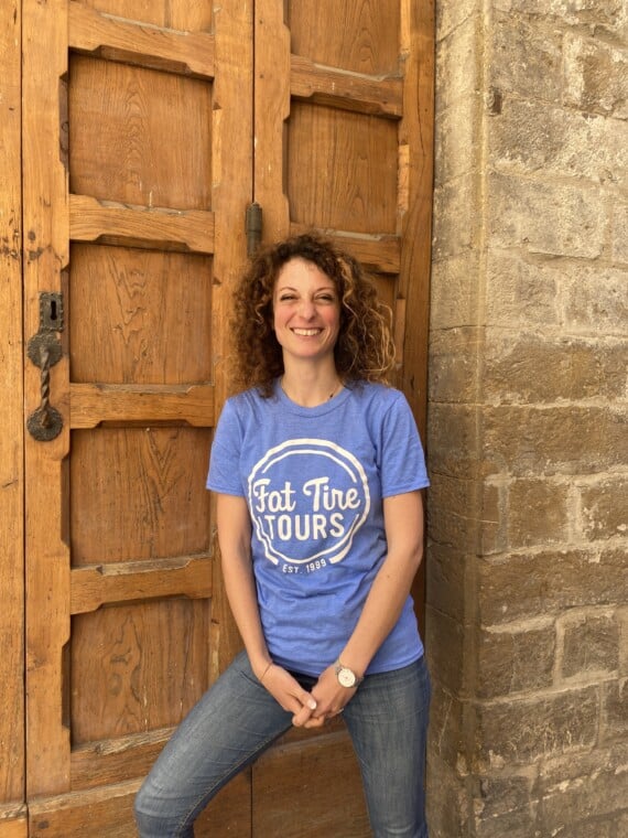 A female in a blue t-shirt leaning against a wooden door and smiling.