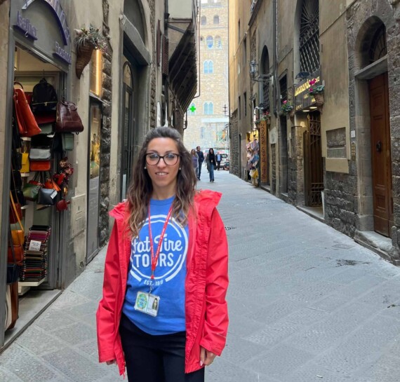 A tour guide in a blue t-shirt and red jacket standing in an empty street in Florence, Italy.