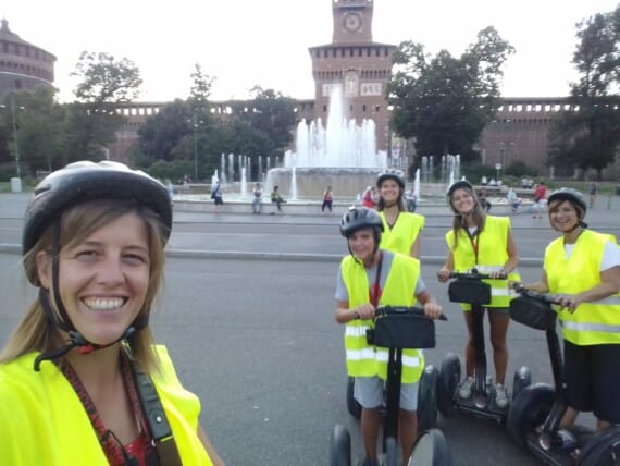 A woman in a high-vis vest and her group of guests on Segways smile for a photo
