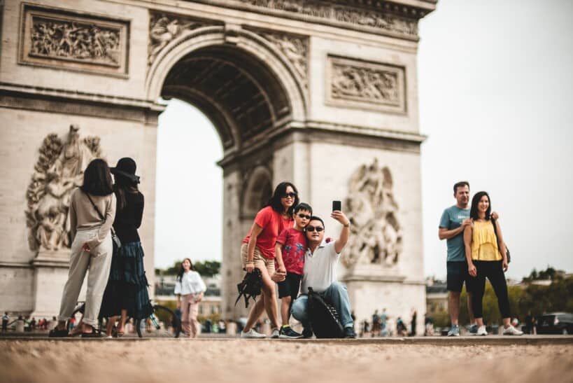 A family of three poses for a selfie in front of the Arc de Triomphe
