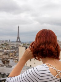 A woman takes a picture of the Eiffel Tower from the top of the Arc de Triomphe