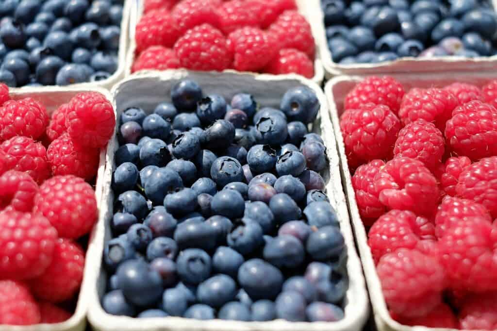 Several baskets of blueberries and raspberries at a market
