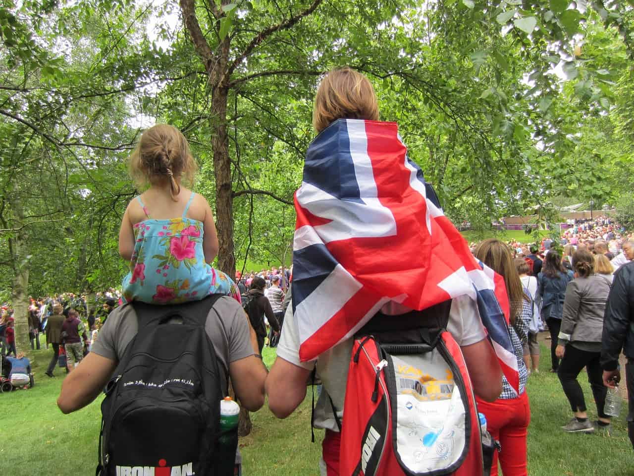 two little kids on their parent's shoulders in a park; one child with the Union Jack flag around him