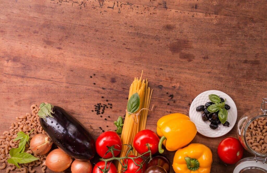 Fresh vegetables and pasta laid out on a wooden table