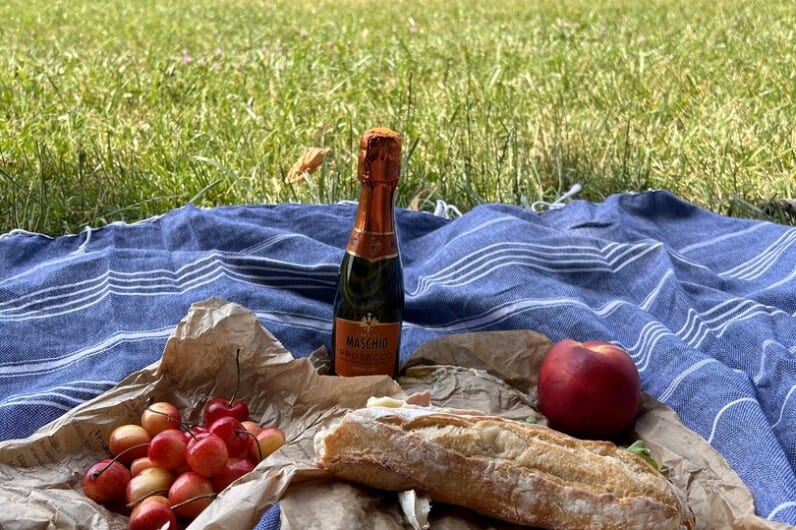 a sandwich, cherries, an apple, and a small bottle of champagne displayed on a picnic blanket
