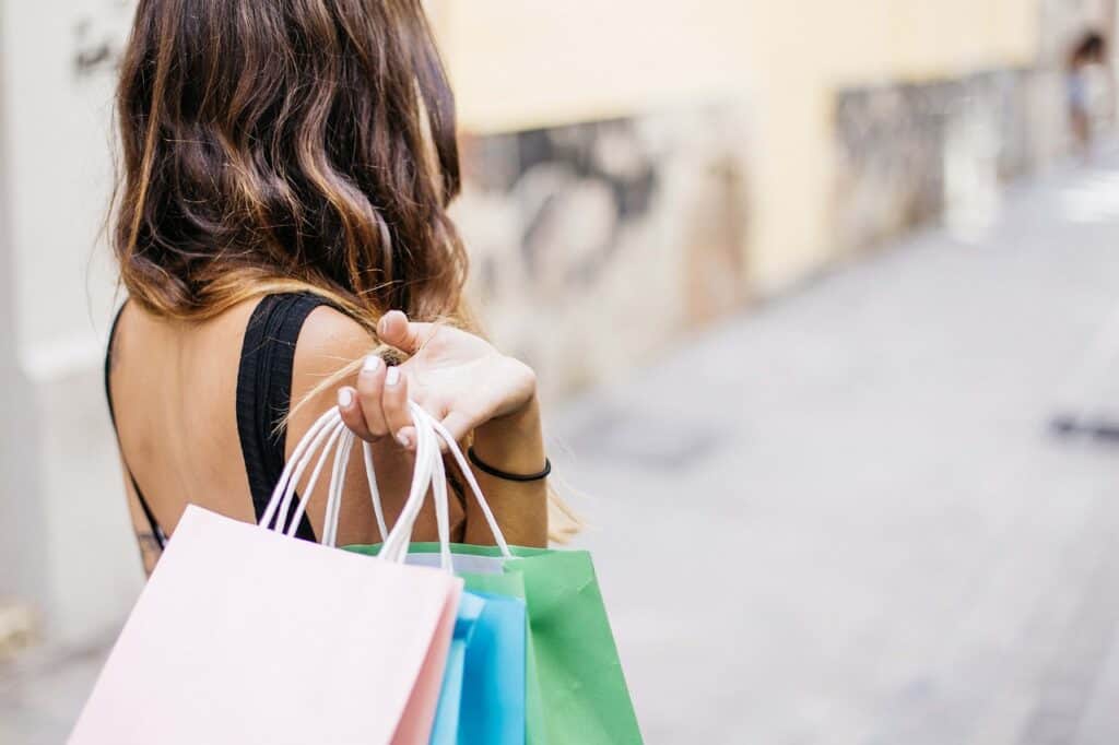 Woman with brown hair carries multiple shopping bags in different colors