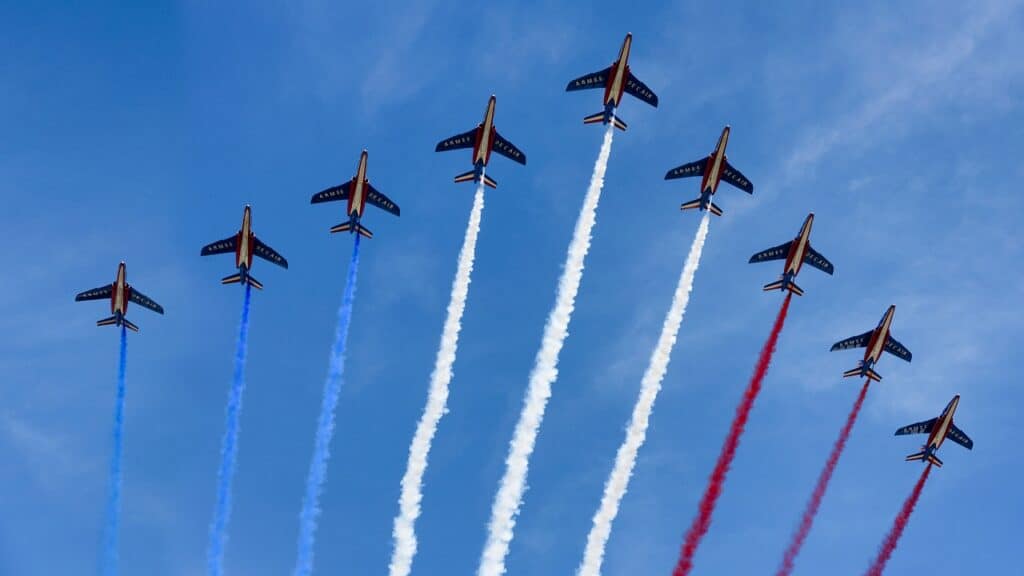 Nine planes are pictured in the sky with colors from the French flag coming out of the back of the planes