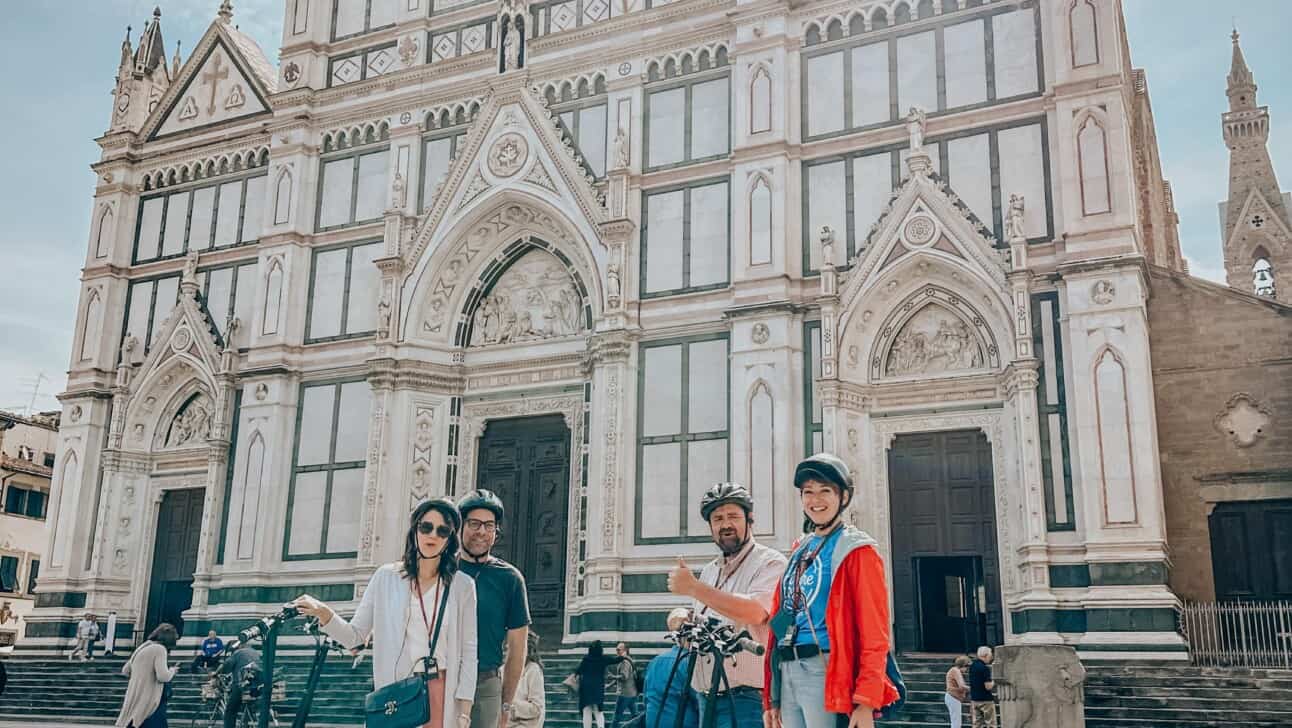 A group of people on e-scooters in front of Santa Croce in Florence, Italy