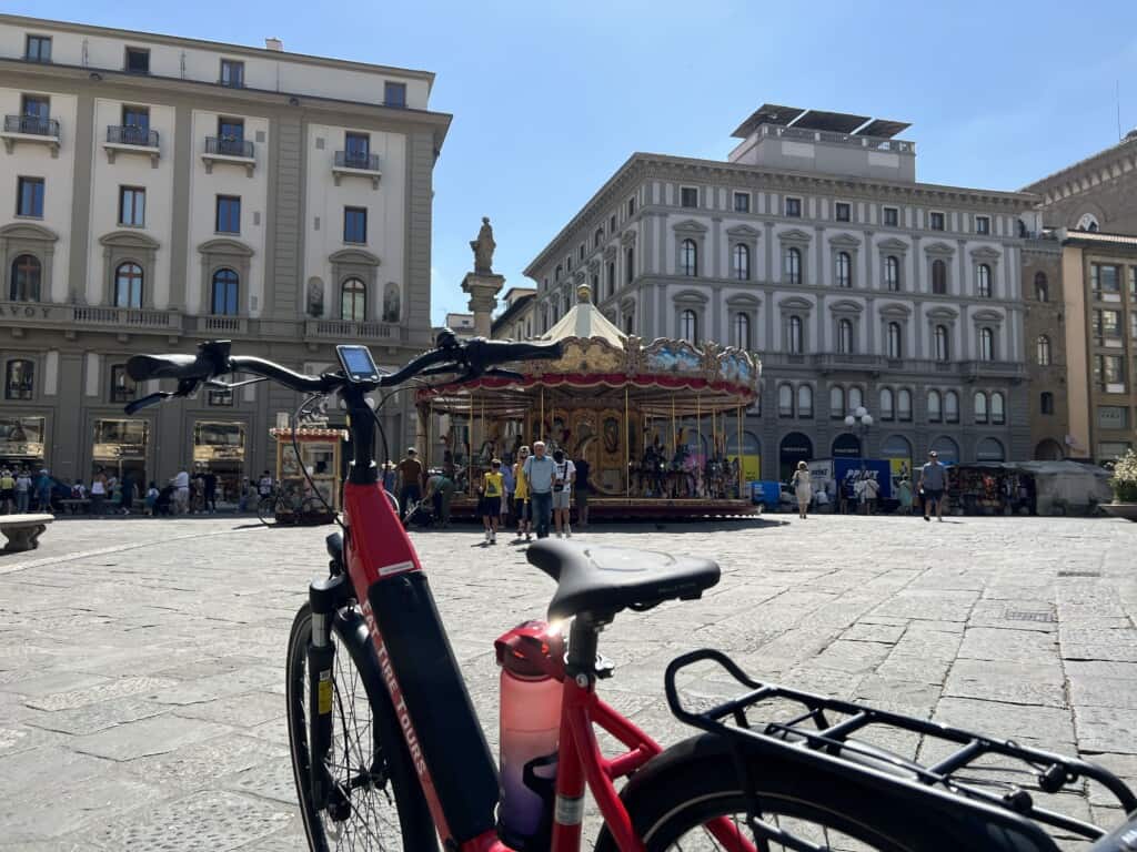 A carousel in a piazza in Italy with a red e-bike in the foreground