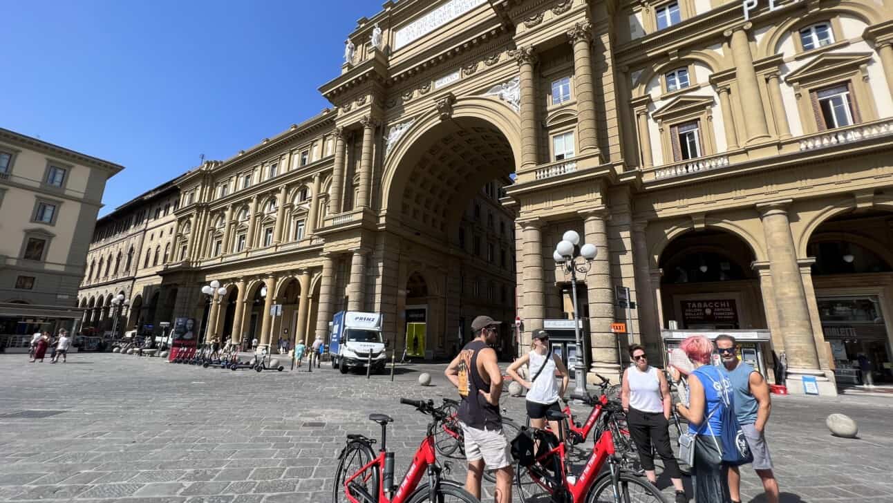 A group of 4 listens to a tour guide in piazza della repubblica in Florence