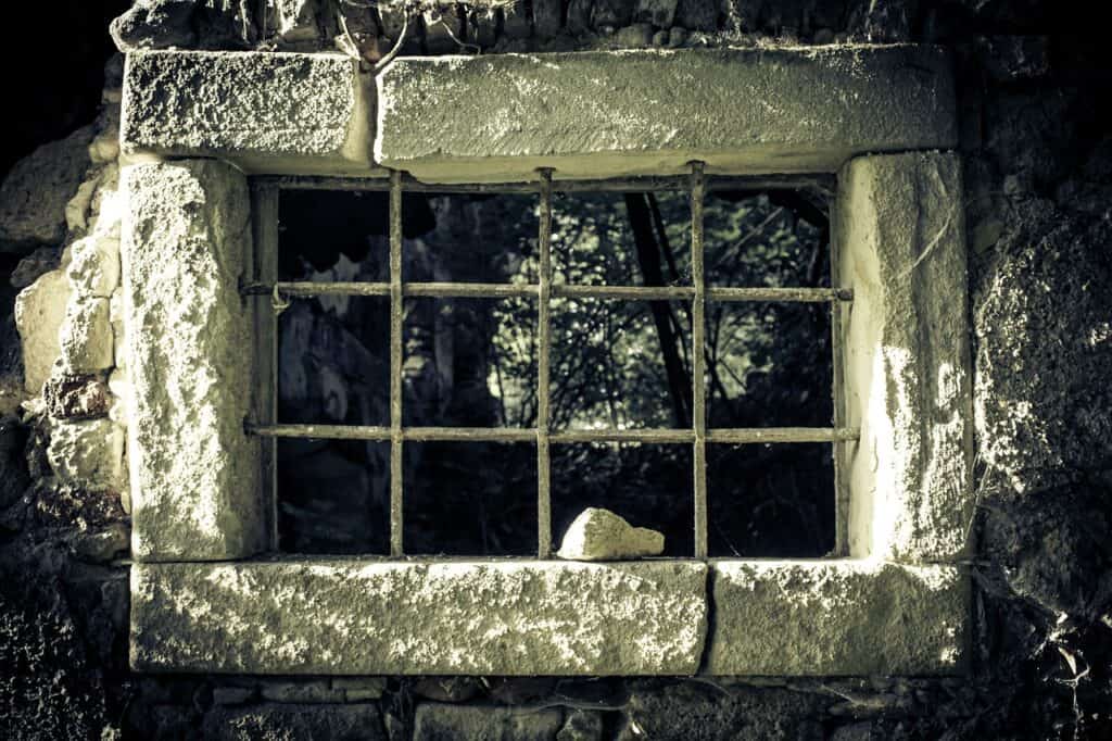 An old jail cell window is shown in a black and white photograph with a stone sitting on the window ledge