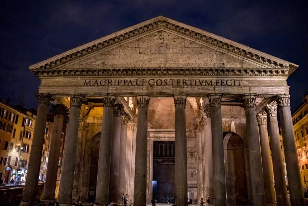 Rome's Pantheon is shown at night with a dark sky and city streetlights behind it