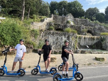 Three men on e-scooters pose for a photo in front of a fountain in Florence, Italy