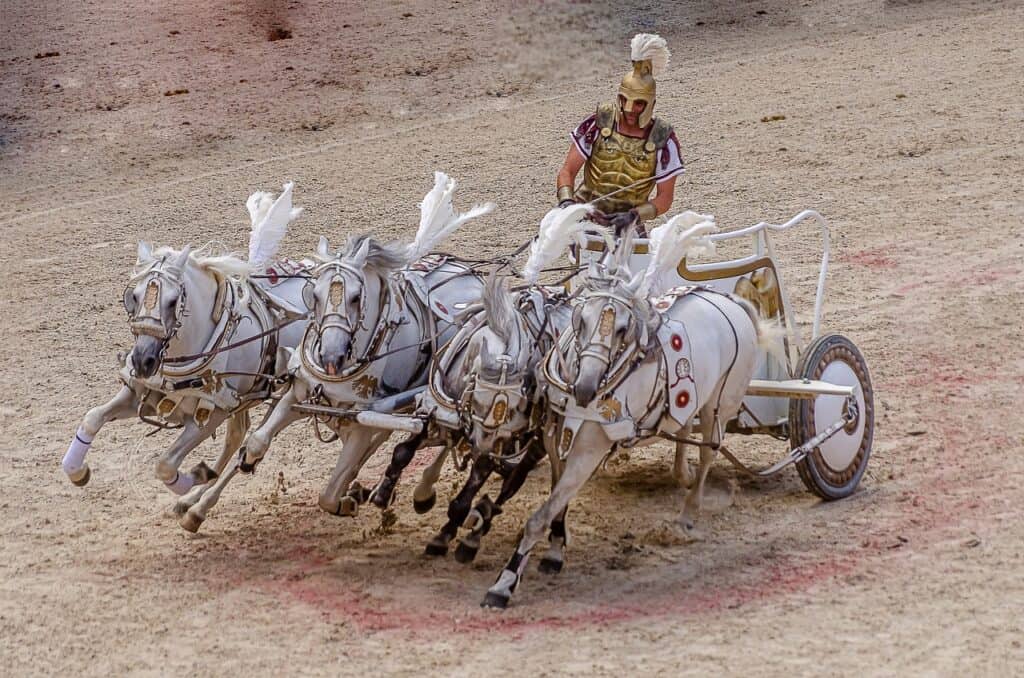 A Roman gladiator rides in a horse-drawn chariot with four white horses pulling him along