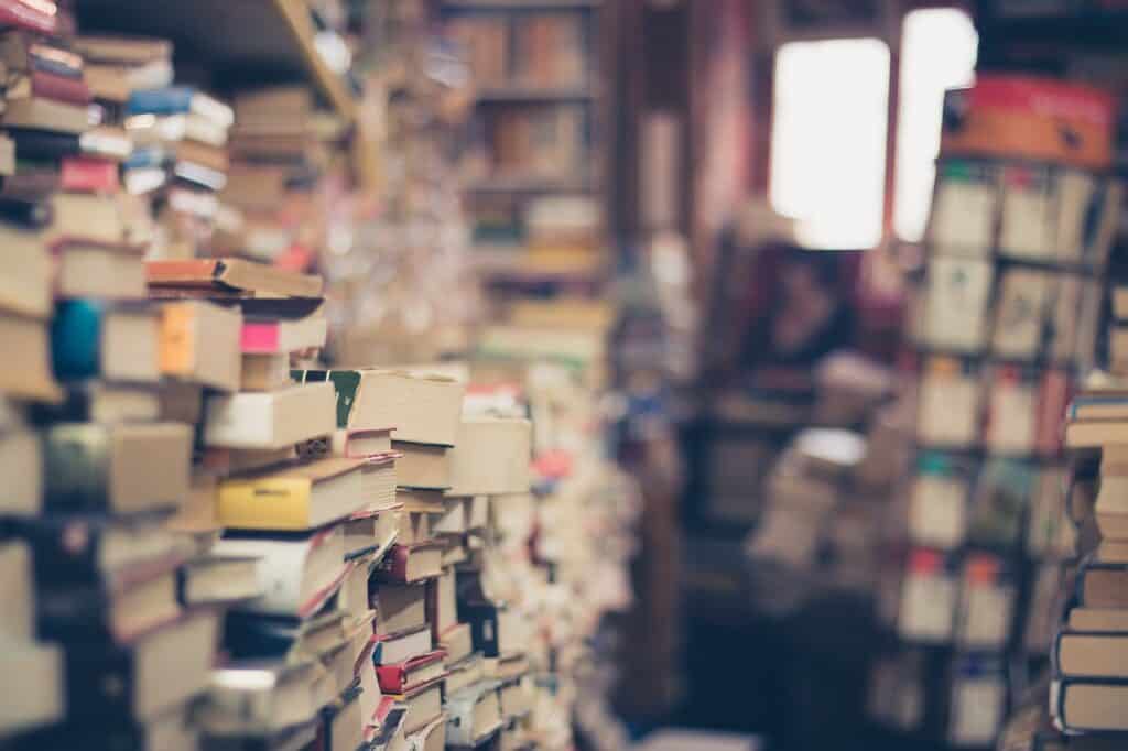 Multiple stacks of books pictured in a library with spines of different colors.