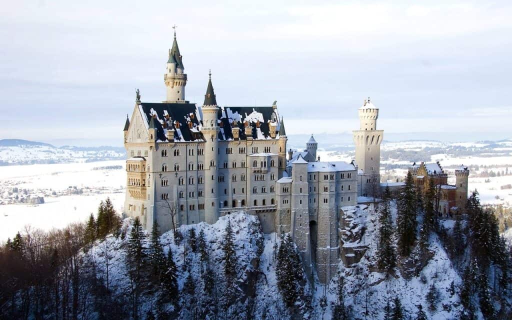 The stunning Neuschwanstein Castle sits on top of a snow-covered hill and has some patches of snow resting on the roof.
