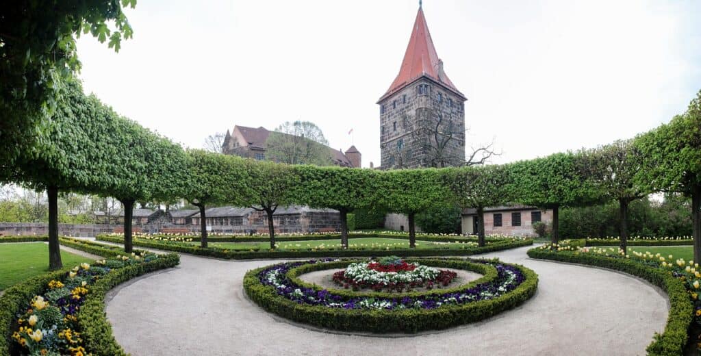 The beautiful grounds at Nuremberg Castle are pictured showing trimmed trees, hedges, and flowers