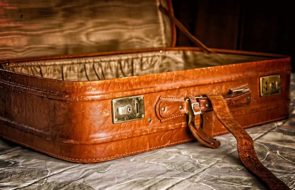 A worn leather suitcase on top of a bed