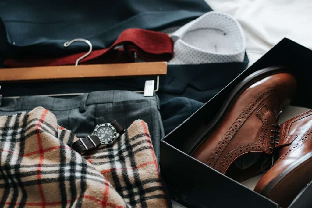 A Burberry scarf and men's shoes and trousers and a shirt laid on a bed