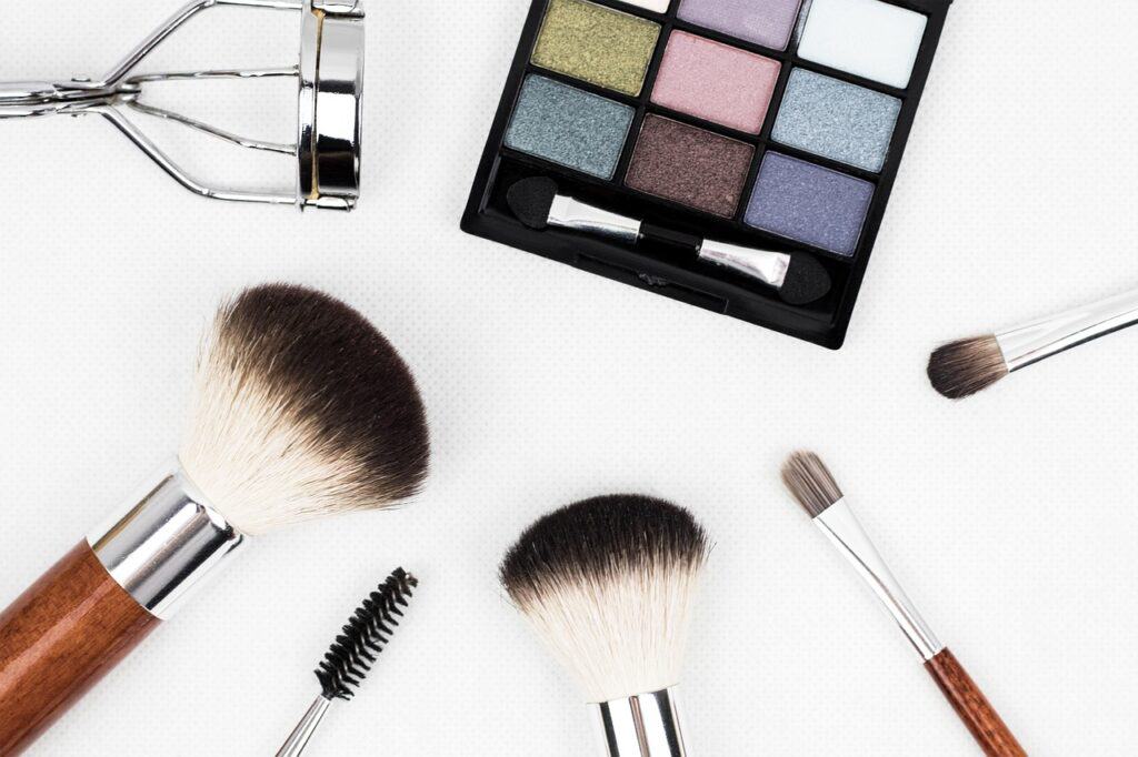 Various makeup brushes and an eyelash curler and eyeshadow palette against a white backdrop