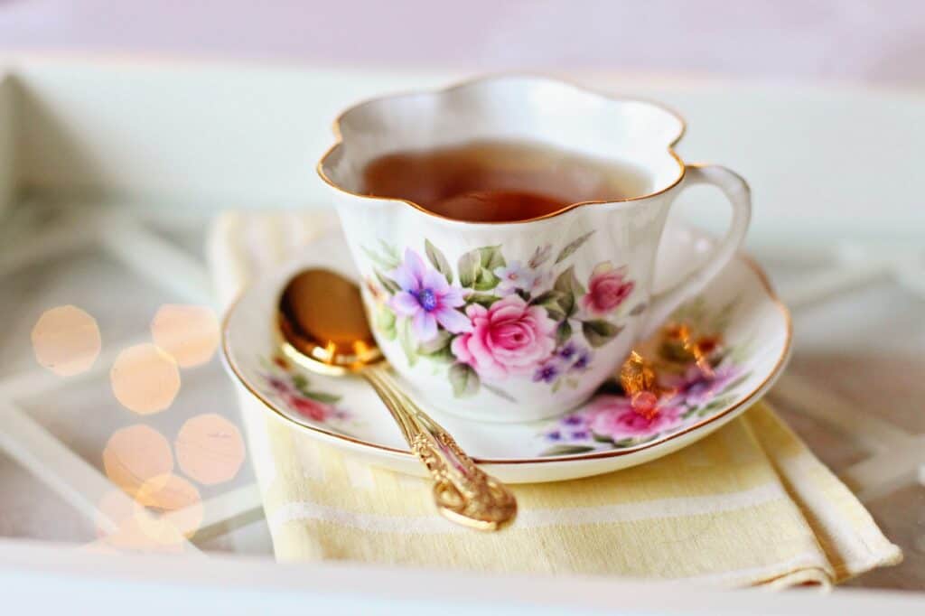 A teacup with flowers on it full of tea with a golden spoon on the teacup plate