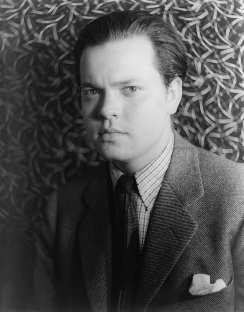 A black and white photo of actor and director Orson Welles with a printed background behind him